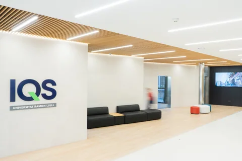 Paneles acústicos decorativos Woodslines: paneles acústicos de madera en bandas de techo del vestíbulo de IQS Barcelona, combinados con iluminación y otros acabados.
